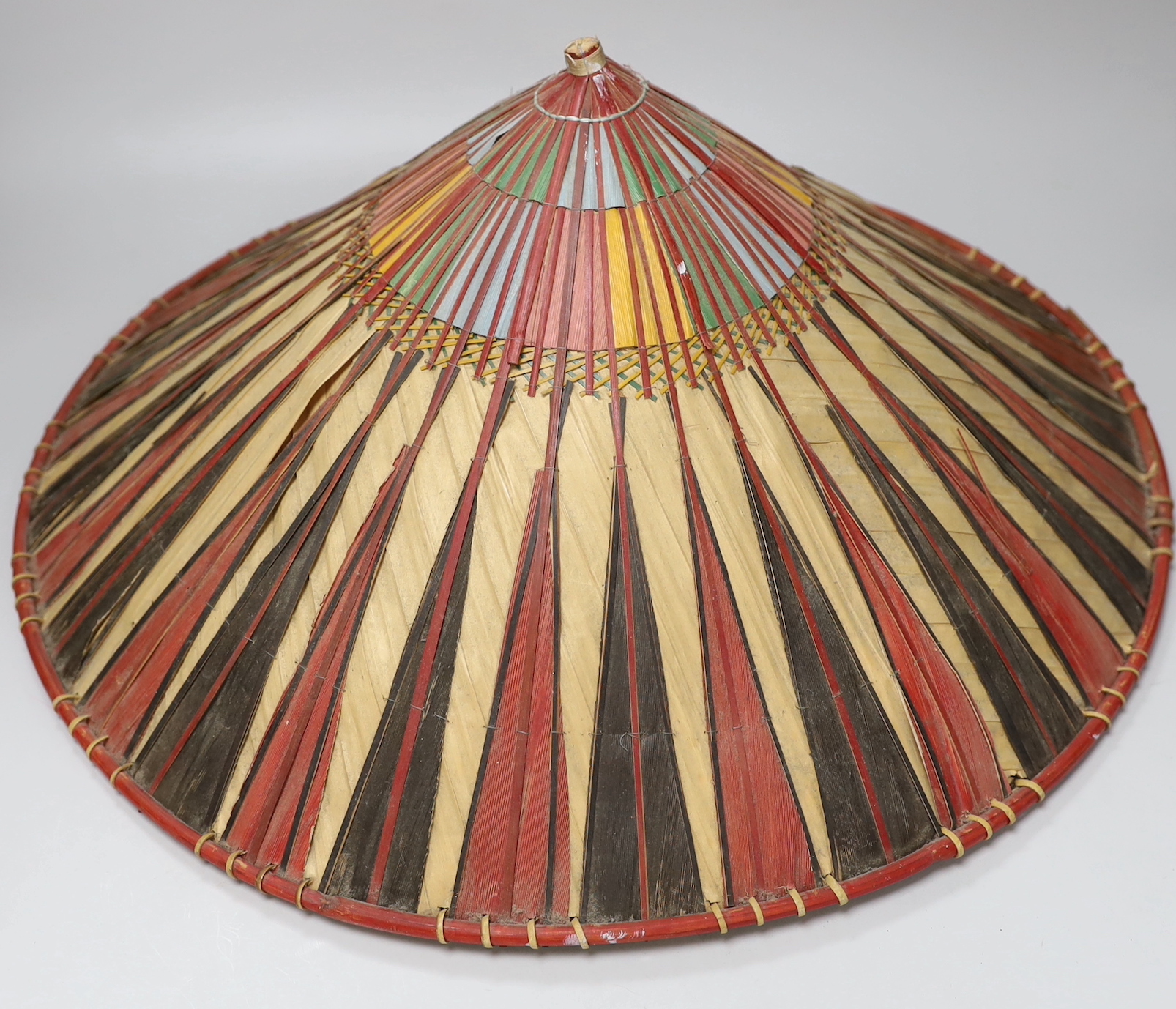 Three red and black striped bamboo rice hats, together with a smaller rice hat with beaded flag decoration